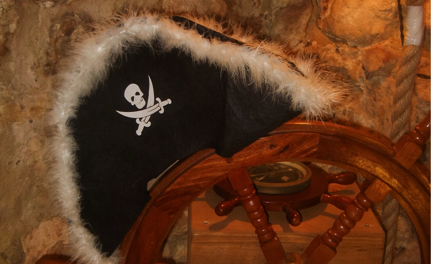 Czapka pirata z futrzanym brzegiem na tle steru okrętu w escape roomie w Krakowie